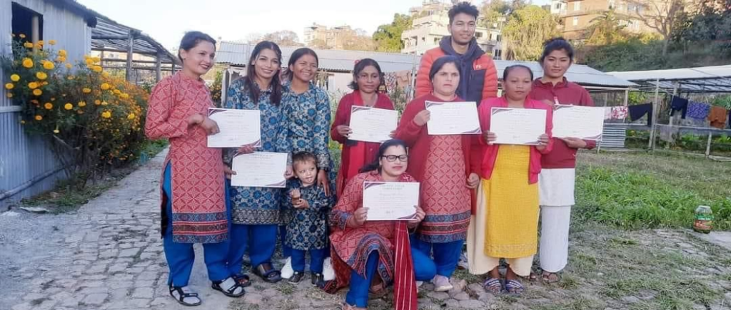 A group of eight women, one young girl, and one man standing together holding certificates, posing for a group photo after completing their training.