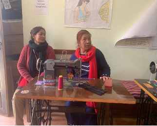 Two women operating a sewing machine.