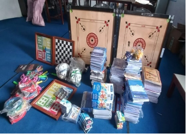 Stationery and sports equipment donations, including a dartboard, Ludo board game, books, notebooks, and pens.